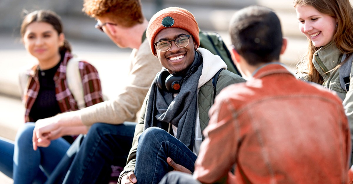 Photo of five students sitting on campus talking